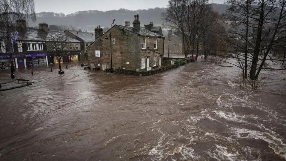 Hebden Bridge town centre under metres of flood water on Boxing Day in 2015. There are rows of stone buildings surrounded by water.