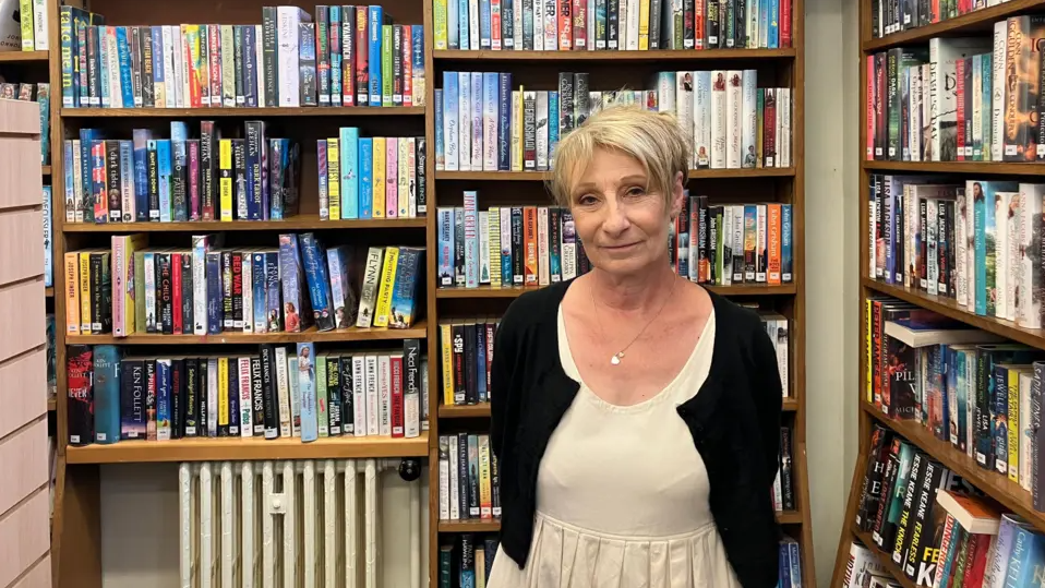 Jennie Storey wearing a black cardigan and white dress - looking at the camera.