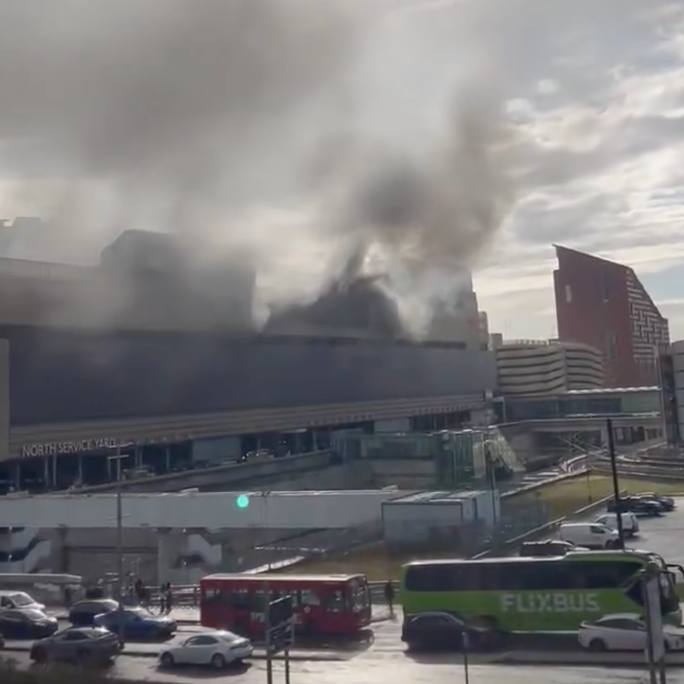 Smoke billowing from the upper area of the multi-storey car park. There are buildings surrounding the area.