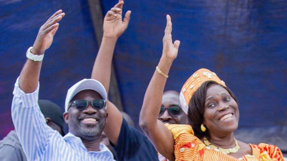 Simone Gbagbo dressed in orange stands to the right of  Charles Blé Goudé  in a stripped blue and white shirt in glasses