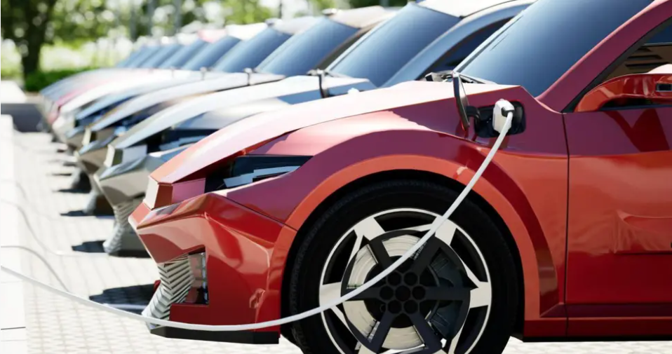 A row of cars parked at electric charging points. The nearest car is red.