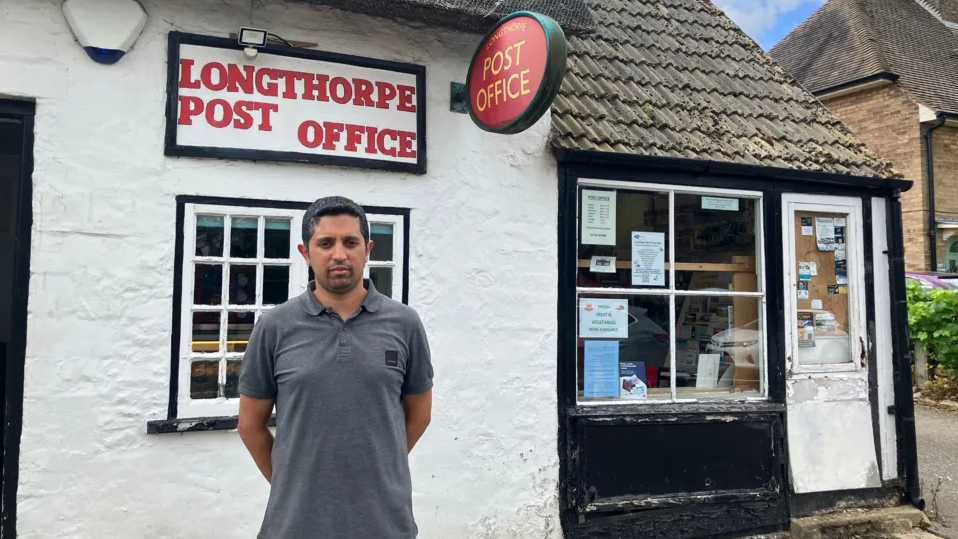 Arif wearing a grey t-shirt standing in front of the Longthorpe Post office 