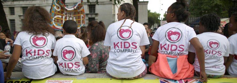 Staff members from the Kids Company charity sit on a wall with children during a rally near Downing Street on August 7, 2015 in London