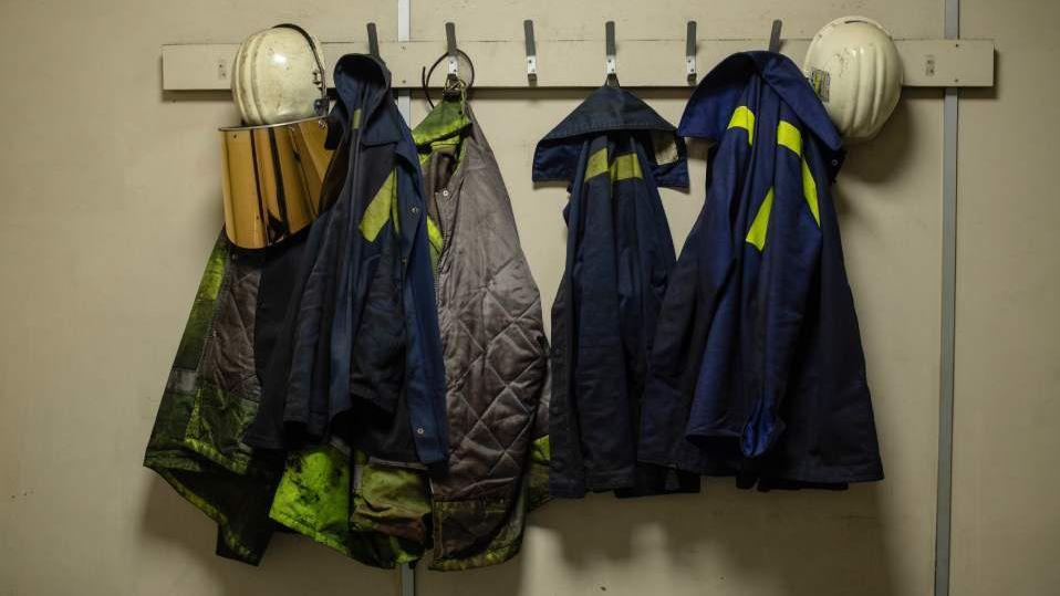 Steelworkers' overalls and helmets are hung on a short row of coat hooks at the Port Talbot site.