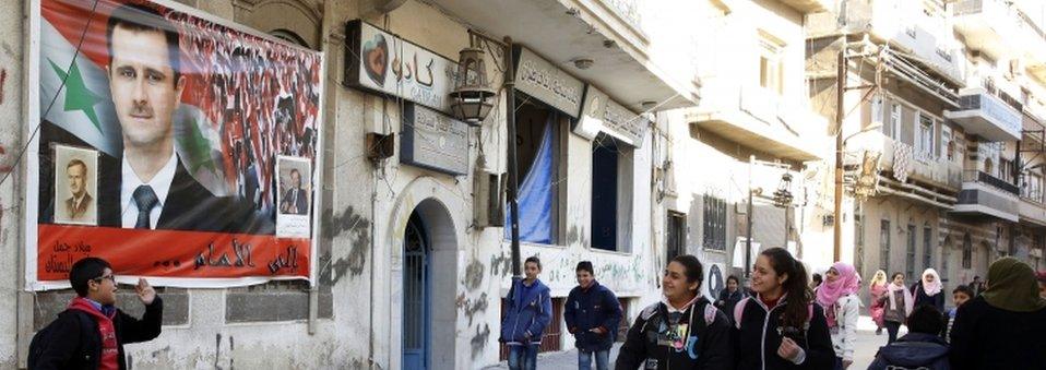 Syrian schoolchildren walk past a poster of President Bashar al-Assad in Homs (8 December 2015)