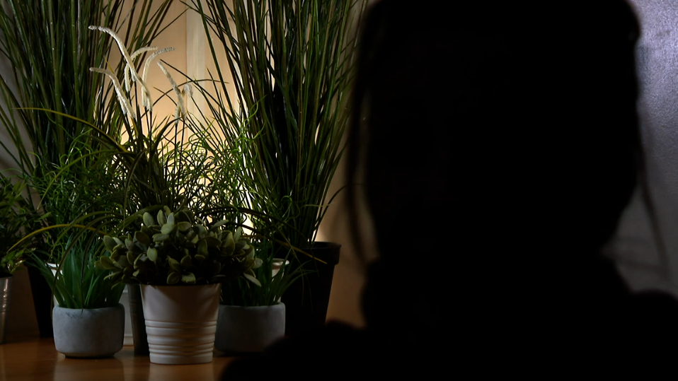 An anonymous victim of Stephen Cox, with her face in darkness to preserve her anonymity, in front of several pot plants in the background as she is interviewed 