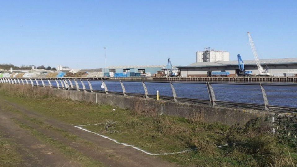 A barren strip of land with a port in the distance across a river.