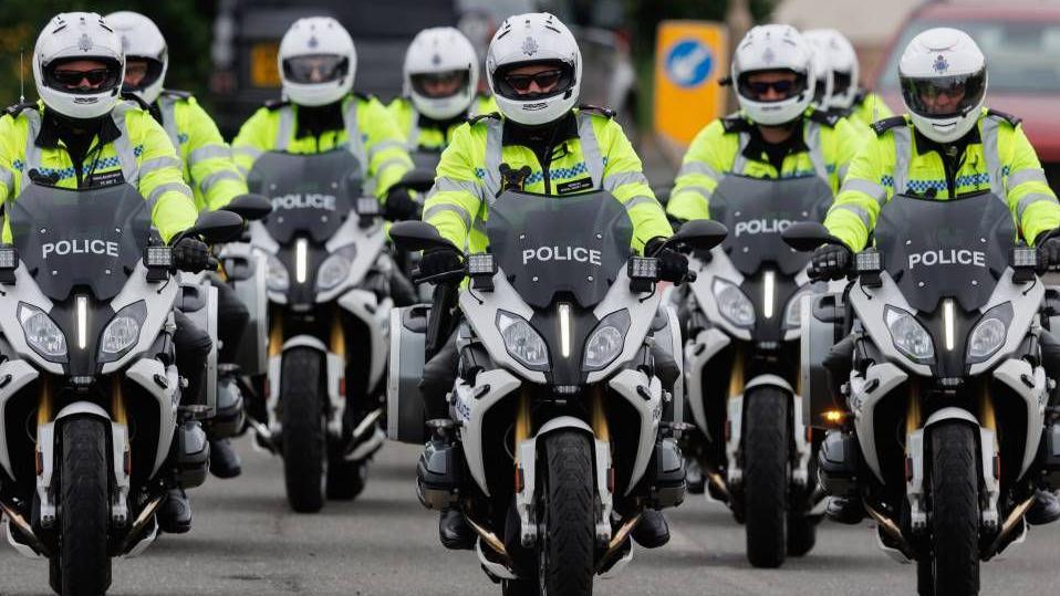 a group of police officers riding motorbikes. They are all wearing white helmets and hi-vis jackets.