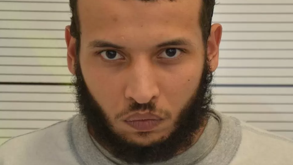 Mugshot of Khairi Saadallah, who had a black beard and moustache, wearing prison-issue grey clothes  