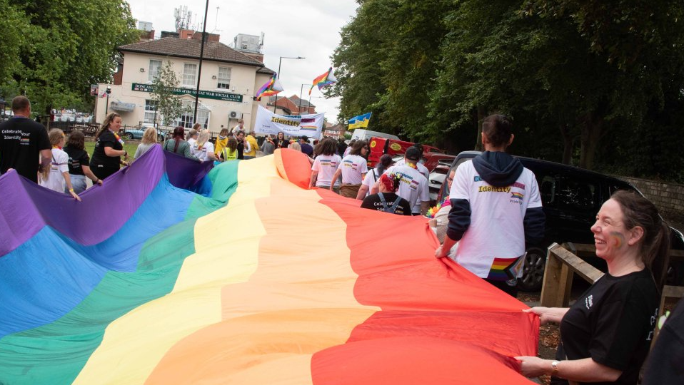 People holding a long rainbow flag stretched horizontally between them as they parade through a Doncaster street