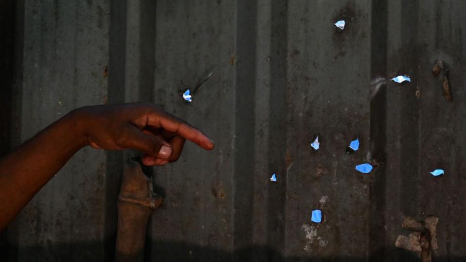 The hand of a Masungi Georeserve ranger is seen pointing at bullet holes on on a metal wall