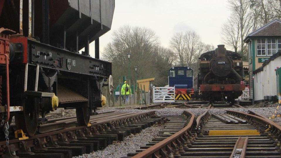 A section of track at Shillingstone station. To the left is a ballast spreader and to the right is the signal box and a black steam locomotive.