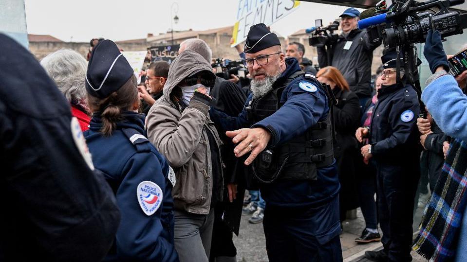 One of the defendants arrives at the court in Avignon, wearing a hood and a facemask to hide his identity