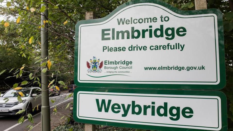 A sign for Elmbridge on the side of a road.
