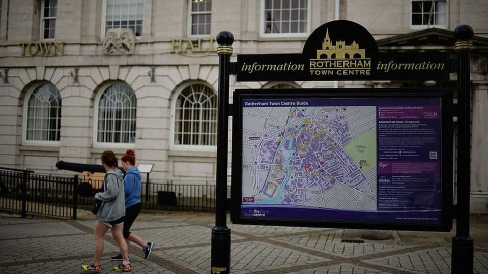 Two girls walk through Rotherham, past the town hall and a town centre map