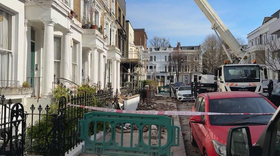 A row of terraced houses with bricks fallen on the pavement. A line of police tape blocks the pavement.