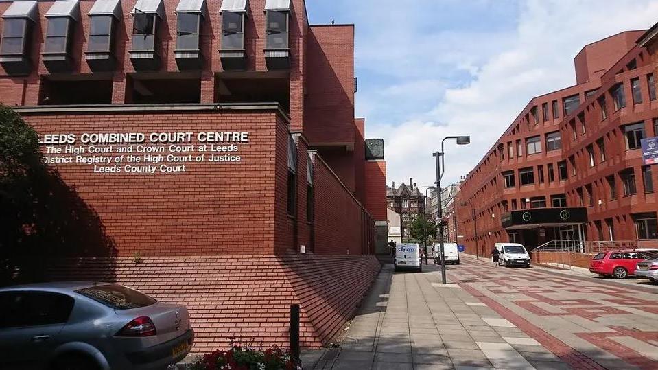 Leeds Crown Court, a red brick building with paved walkway outside and a few cars parked nearby. 