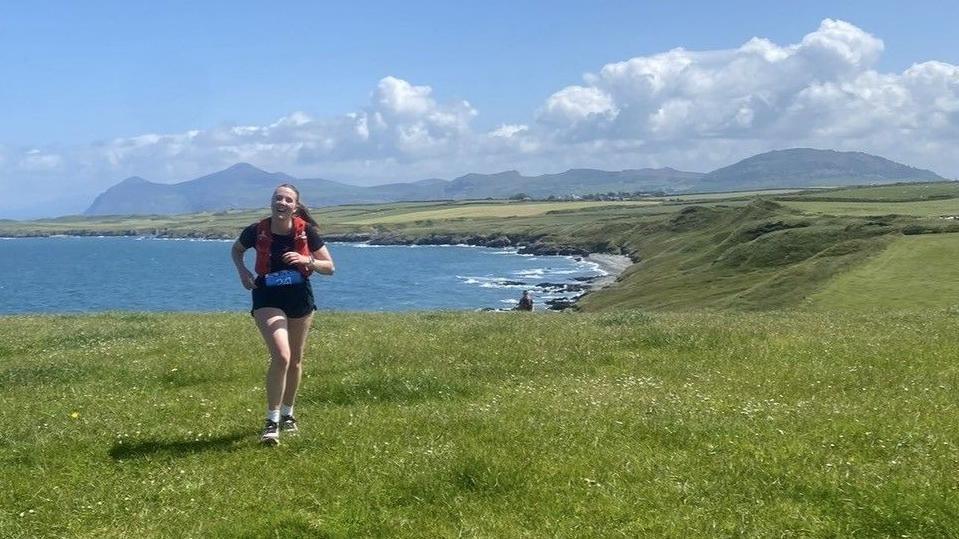 Catrin yn rhedeg gyda golygfa o'r mor a'r mynyddoedd yn y pellter