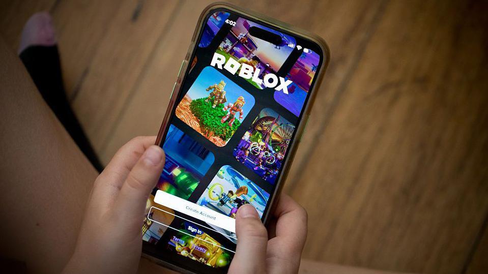 a young person holding a phone with roblox on it