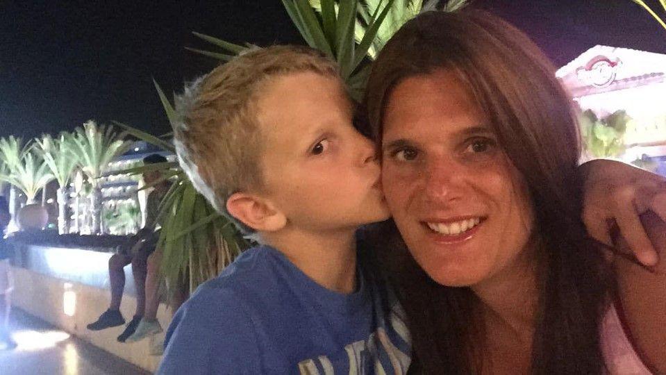 A little boy wearing a blue t-shirt kisses his mum on the cheek and she smiles to the camera.