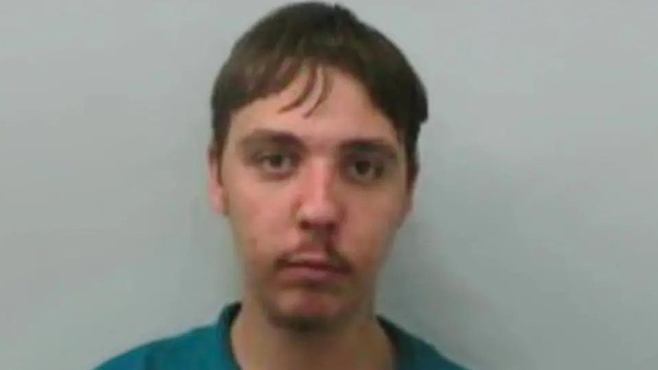 Jason looks blankly at the camera in a police custody image. He has dark hair, eyebrows, and a faint moustache
