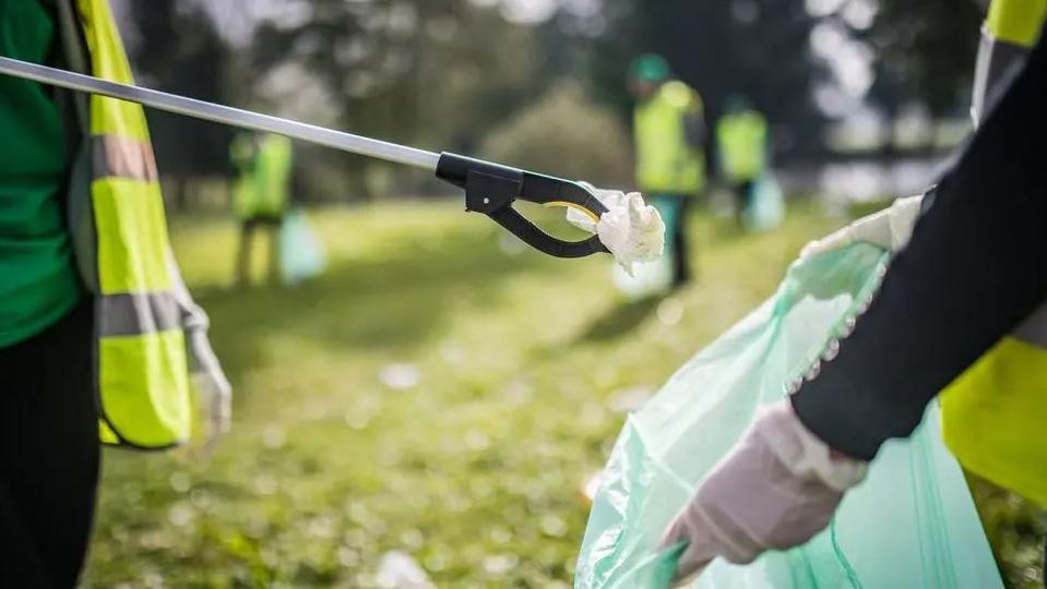 A generic image of two people holding a litter picker and a clear plastic bag outside.