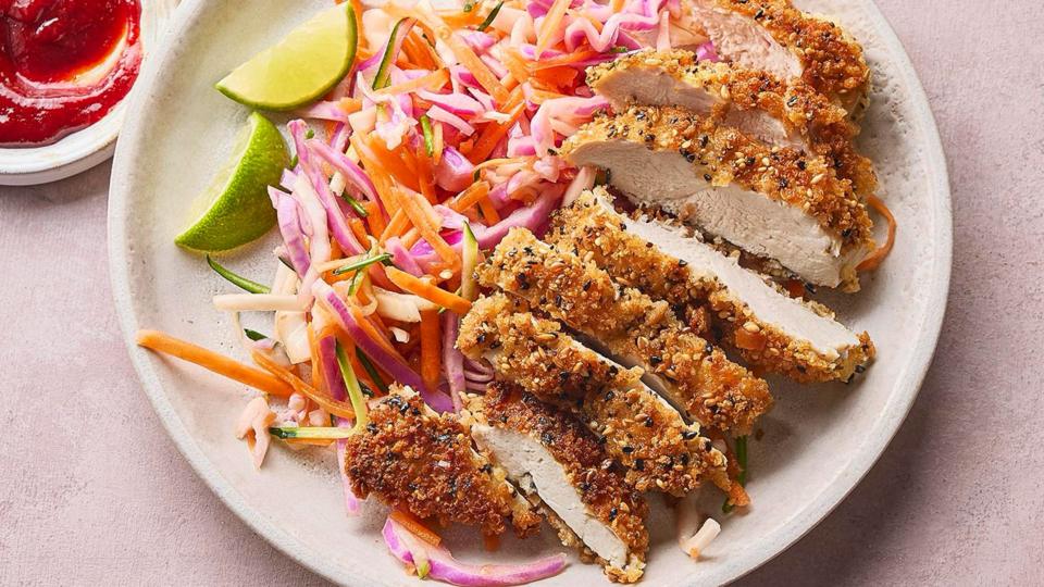 A plate with crispy fried chicken sliced up, next to coleslaw and lime wedges.