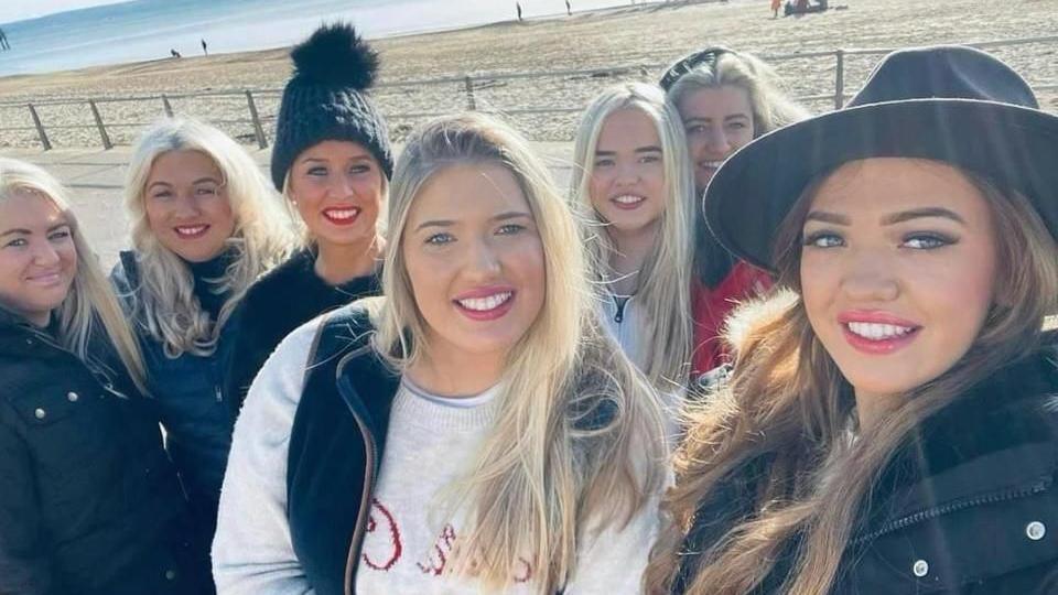 Tracy Lewis with six of her adults daughters. All the women have long blonde hair. Bournemouth's sandy beach and the sea are in the background.