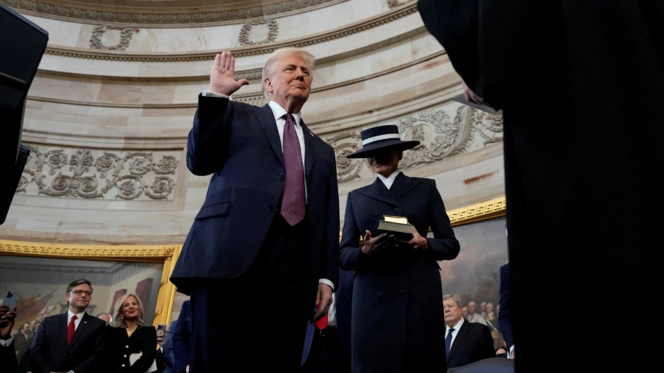 Trump angle from the bottom down with hand raised as he takes oath of office. Melania Trump just behind him holding Bible