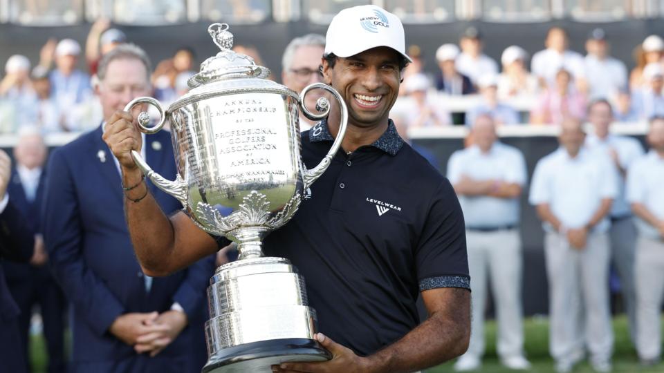 Aaron Rai holds a large silver trophy smiling