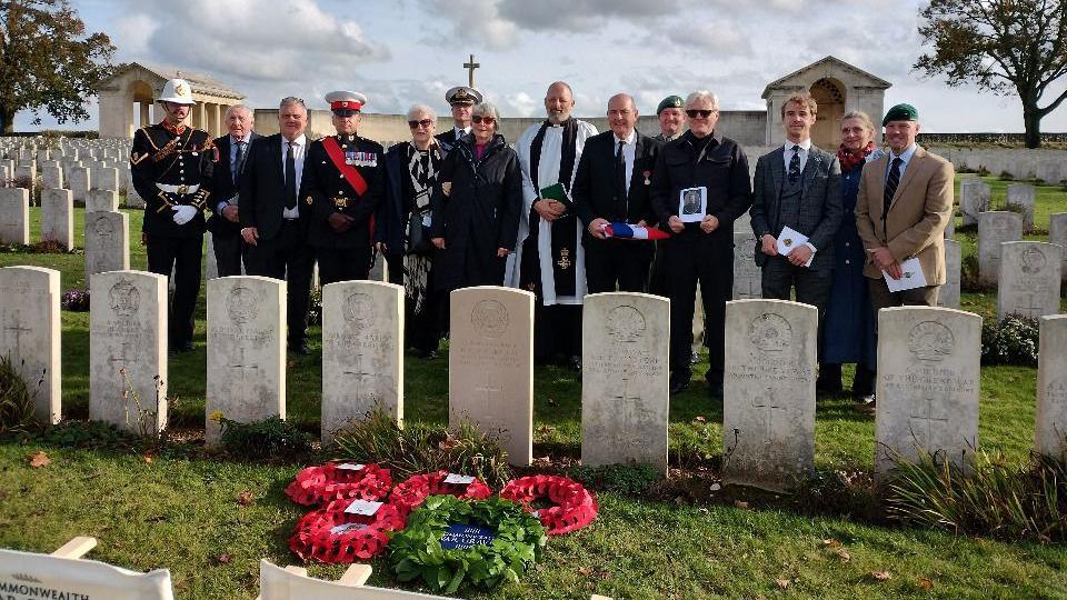 A group of people stand in front of a grave.