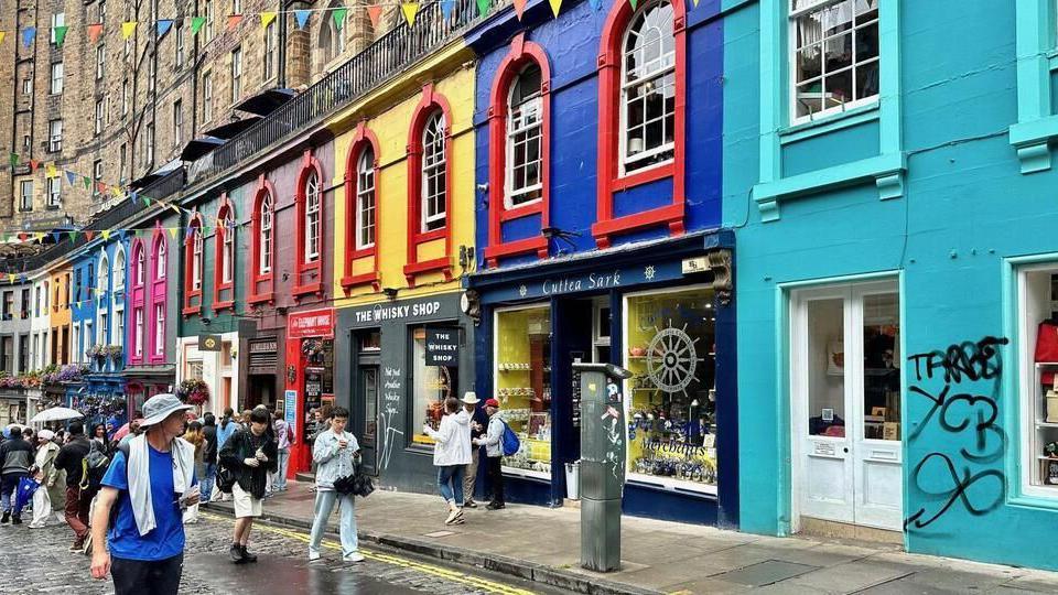 Colourful buildings painted all different colours and a cobbled road in front with tourists walking on it.