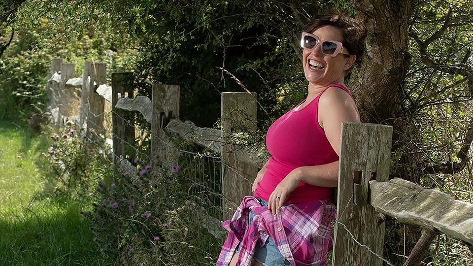 Image showing a woman in a pink top leaning against a fence and smiling at the camera