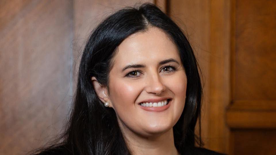 Claire Sugden is smiling at the camera, she has long dark hair and is wearing a black blazer.