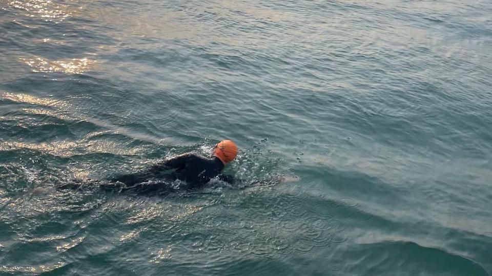A man in a wetsuit, wearing an orange swimming cap 