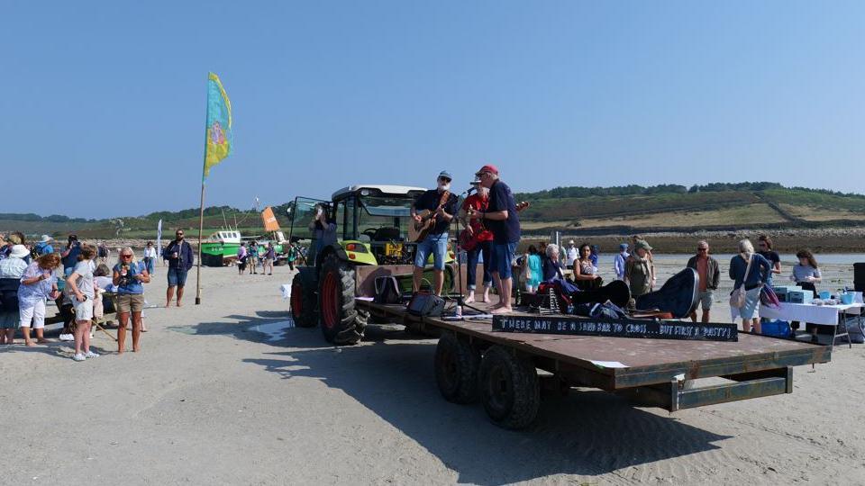 A folk band can be seen performing on a trailer that is being pulled by a tractor.