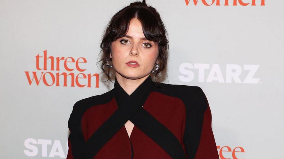 Gabrielle Creevy looks at the camera and wears a maroon and black top. She has silver earrings in and her dark hair is tied in a bun.