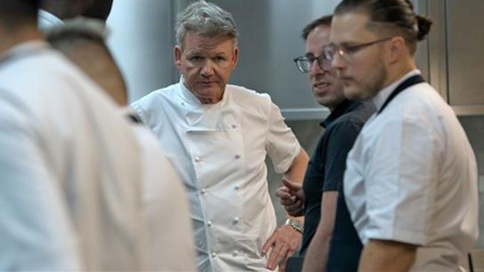 A still from ‘Being Gordon Ramsay’ where Gordon is stood in a kitchen surrounded by various chefs.