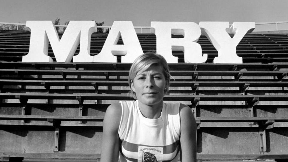 Mary Rand poses in front of a sign saying Mary