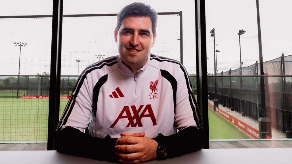 New Liverpool manager Andoni Iraola in white and black club training kit with red lettering, sitting at a table at the club's training ground