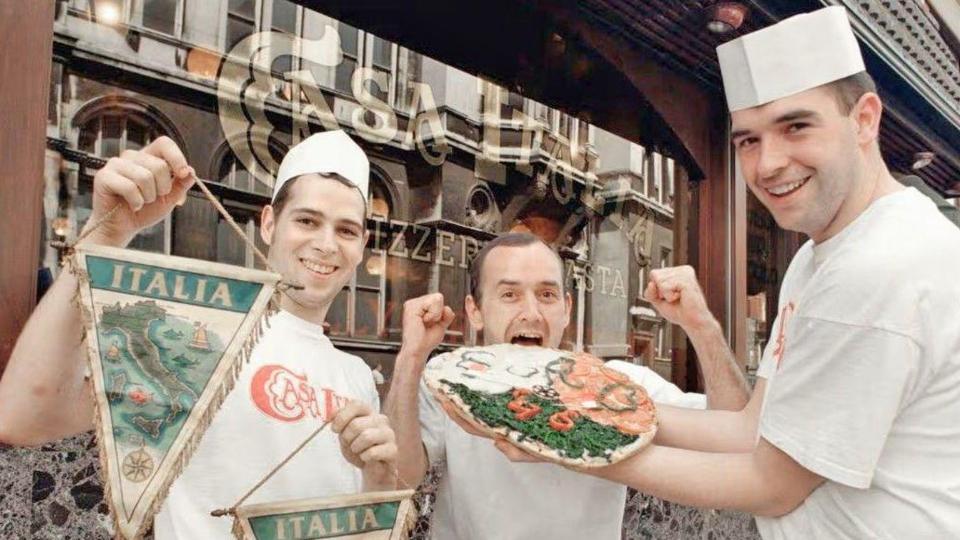 Casa Italia staff hold pizza and a sign.

