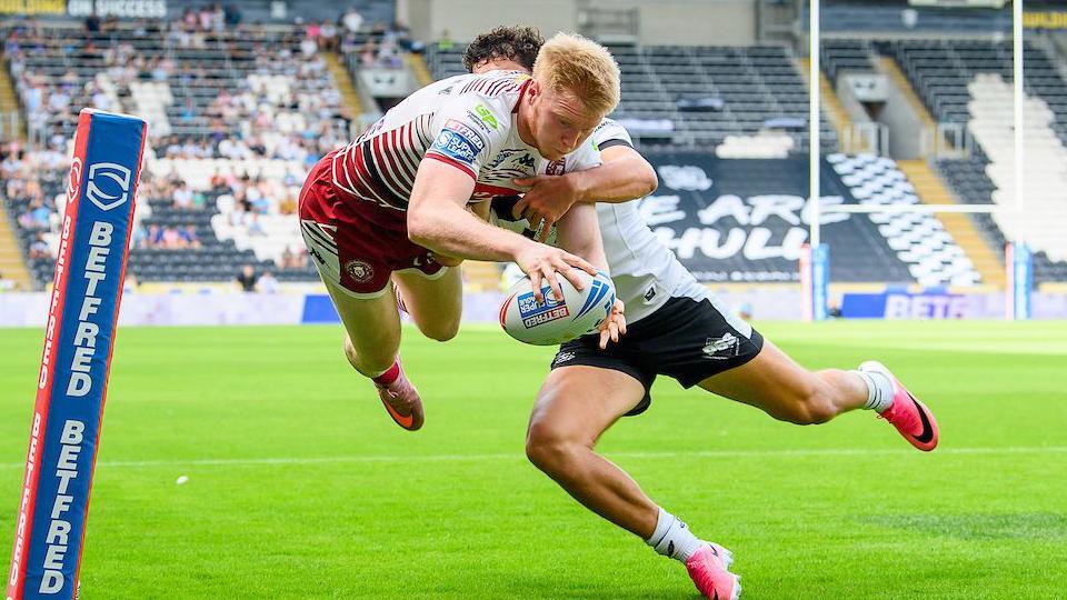 Wigan's Zach Eckersley leaps in the air while challenged by a Hull player to score a one-handed try