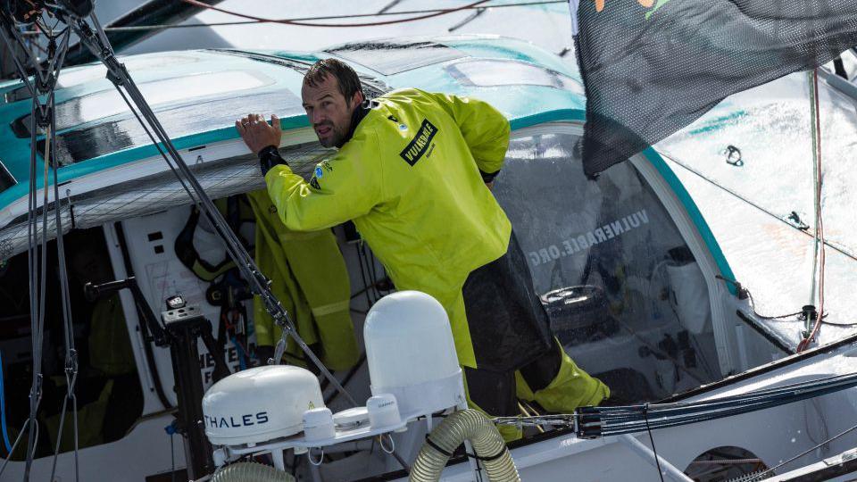 A yacht skipper in a yellow sailing suit in the cockpit of a yacht.