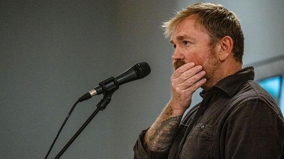 Graham Platner seen on stage at a microphone. his hand is over his mouth 