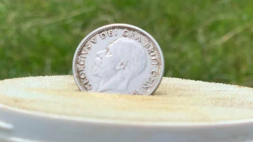 A George V silver coin displayed outdoors on a soft surface.