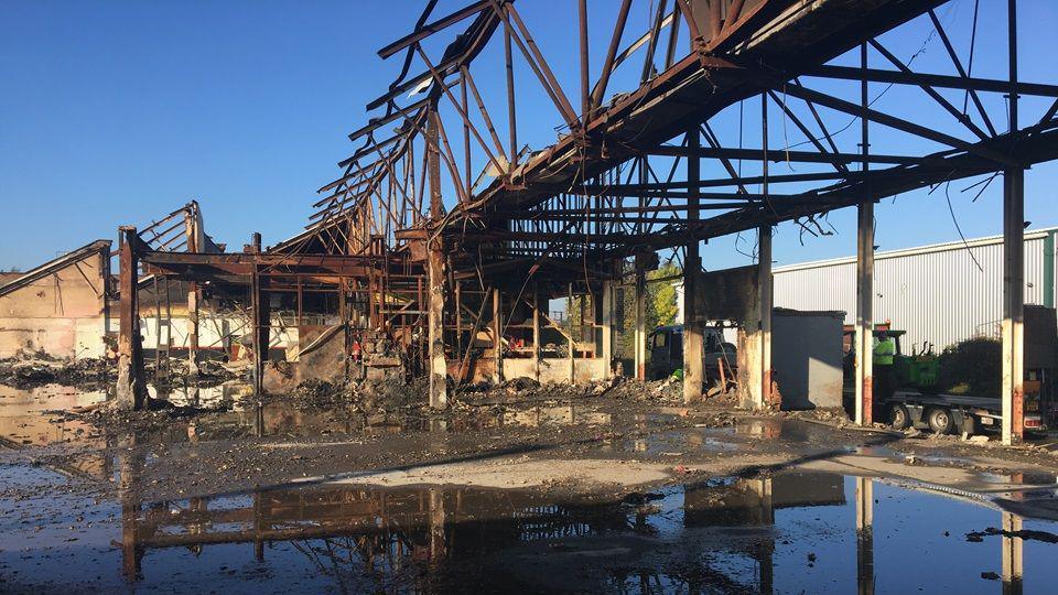 The rusty frame of a building which burnt items in the background.