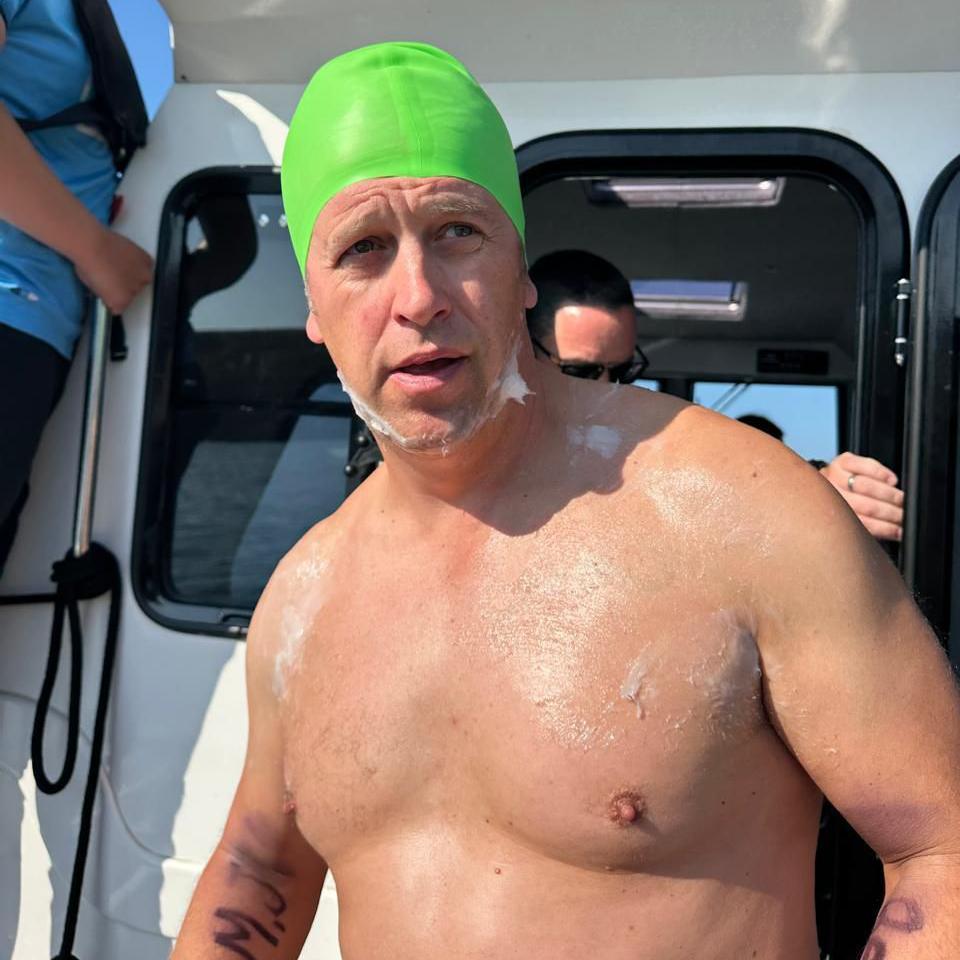 A man in a green swimming cap on a boat, without a shirt on.