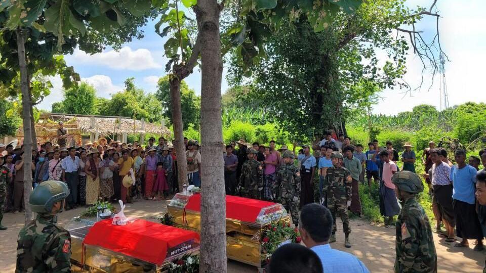 Two coffins sit on the ground as a crowd looks on