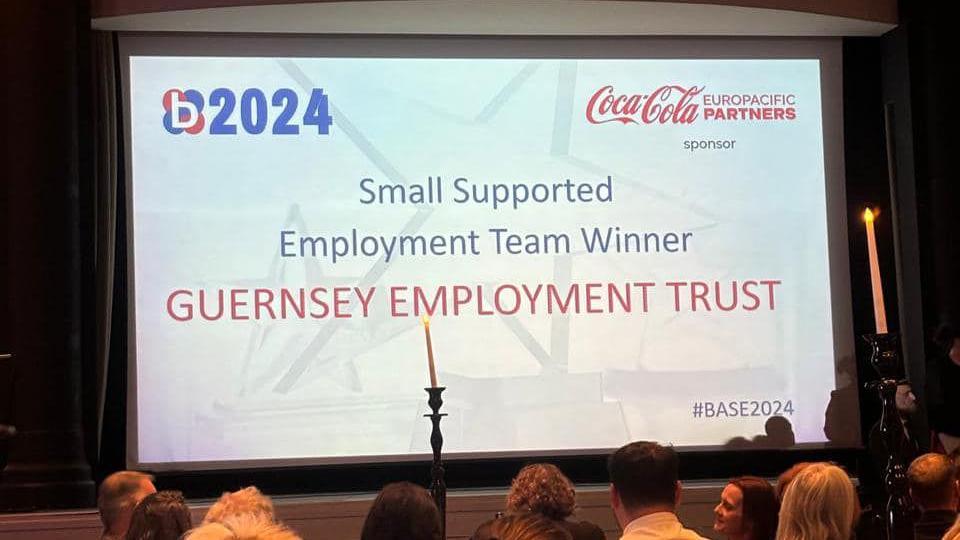 The screen at the awards ceremony which has '2024' in the top left corner. At the centre are the words 'Small Supported Employment Team Winner Guernsey Employment Trust'. In the bottom right corners are the words '#BASE2024'.