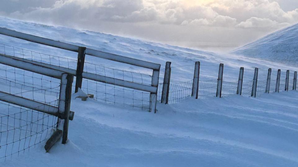 A fence that is half buried in snow on the side of the Mountain Road.